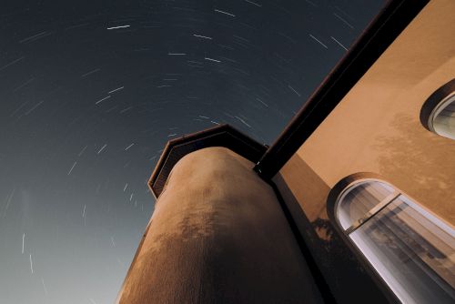 The image shows a building taken from a low angle at night, with star trails visible in the sky, indicating long-exposure photography.