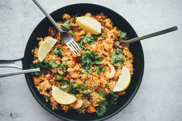 A pan filled with rice dish, garnished with lemon wedges, cilantro, and several forks.