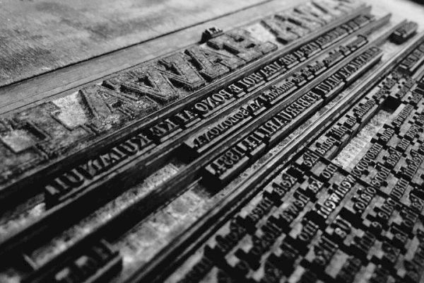 This image shows a vintage letterpress setup with metal type arranged for printing text. The letters and words are placed in reverse for printmaking.