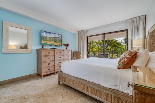 This image shows a well-furnished bedroom with a large bed, a chest of drawers, a wall-mounted TV, a mirror, and a scenic view through a glass door.