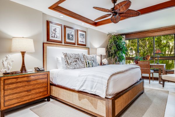 A cozy bedroom with a stylish bed, wooden nightstands, lamps, framed pictures, indoor plants, a ceiling fan, and a scenic view from large windows ending the sentence.