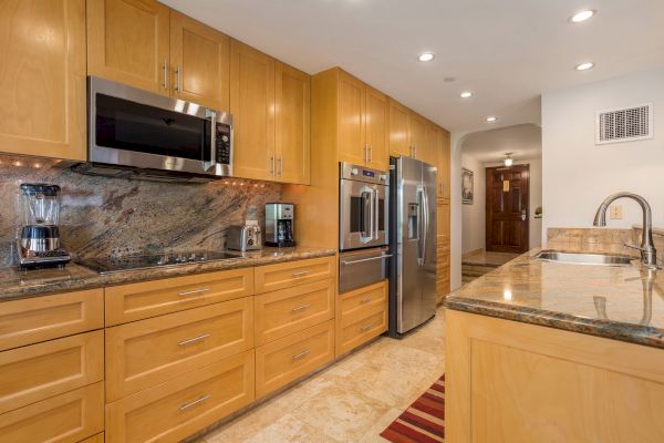 This image shows a modern kitchen with wooden cabinets, stainless steel appliances, a marble countertop, a coffee maker, and a microwave.