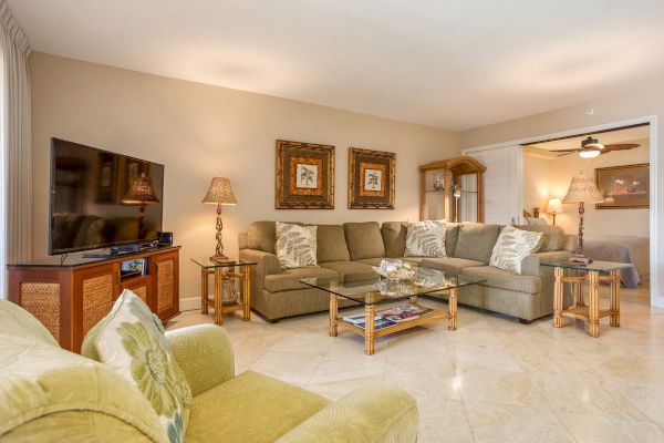 A cozy living room with a large sectional sofa, glass coffee table, flat-screen TV, decorative lamps, and framed art on the walls.