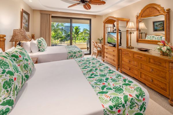 A hotel room with two beds featuring tropical-themed bedding, wooden furniture, a ceiling fan, a TV, a dresser, a mirror, and a balcony view.