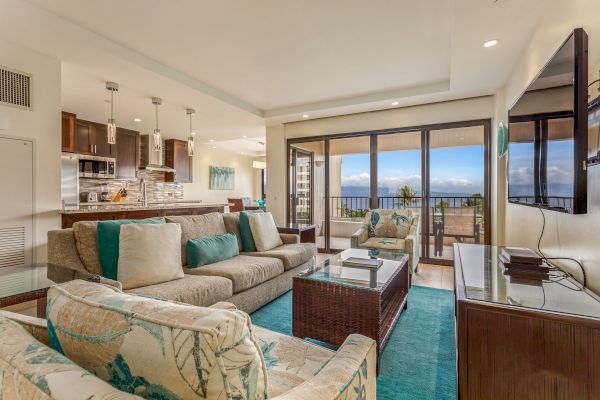 A modern living room with beige furnishings, teal accents, a flat-screen TV, open kitchen, and balcony with ocean view always ending the sentence.