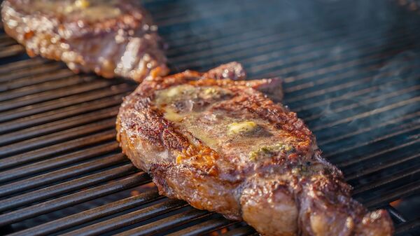 Two ribeye steaks are grilling, with melted butter on top, creating a delicious, sizzling appearance on the barbecue grill.