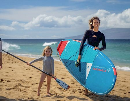 Three people, two adults and a child, pose on a beach with paddleboards, ready for stand-up paddleboarding.