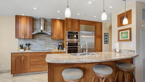 A modern L-shaped kitchen with wooden cabinets, granite countertops, stainless steel appliances, an island with a sink and seating.