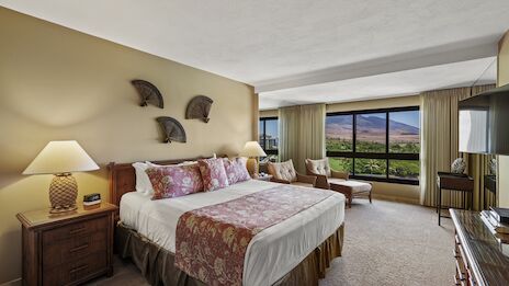 A hotel room with two beds, decorative pillows, bedside lamps, a seating area, and a large window offering a landscape view.