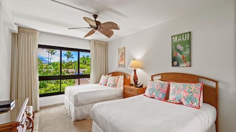 A bright hotel room with two queen beds, tropical decor, a ceiling fan, large window with curtains, and a view of palm trees outside.