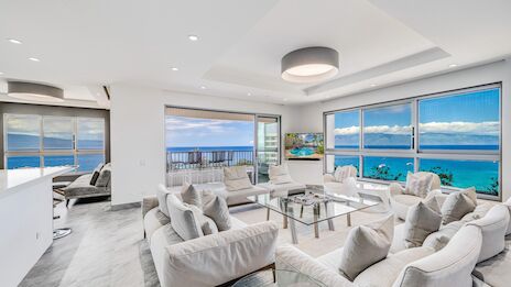 Luxurious oceanfront living room with white sofas, glass coffee table, panoramic windows, and a bright airy vibe over the sea.
