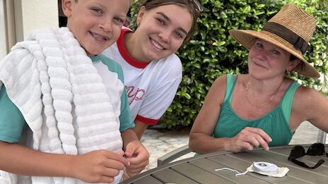 Three people at an outdoor table with two board games, one wearing a towel, another in a hat.