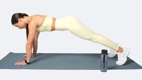 A woman in athletic wear performs a plank on a yoga mat, with a water bottle beside her, focusing on fitness and form.