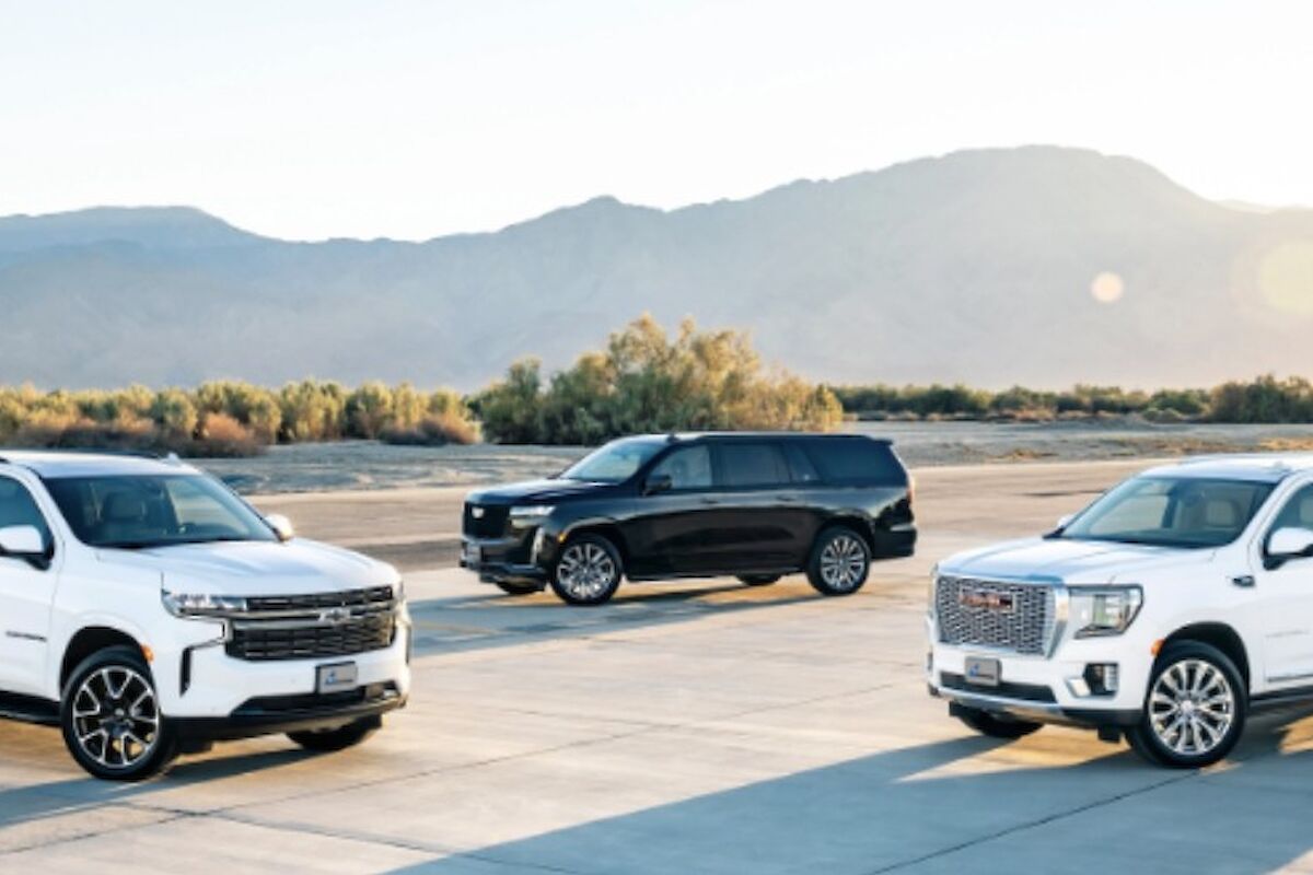 Three SUVs parked on a tarmac with desert scenery and mountains in the background, white and black vehicles under sunny sky.