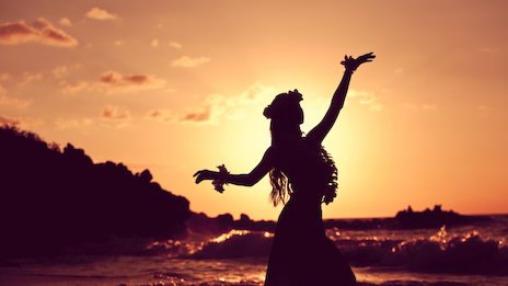 A silhouette of a person dancing gracefully on the beach at sunset, with warm orange hues and waves in the background. Ending with a period.