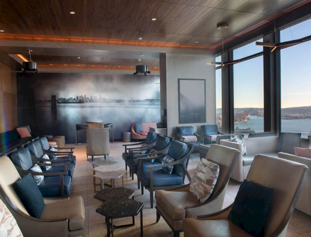 A modern lounge with comfy seating arrangements, large windows offering scenic views, and a city skyline mural on the wall.