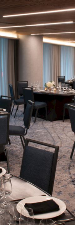 A banquet hall with round tables set for a formal event. Tables are decorated with flowers, candles, and place settings.