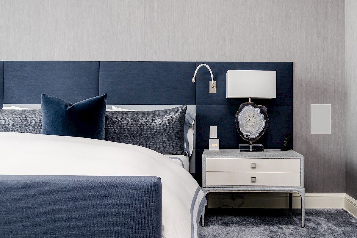 A modern bedroom with a blue bed, a white nightstand, a lamp, and a decorative item on the nightstand.